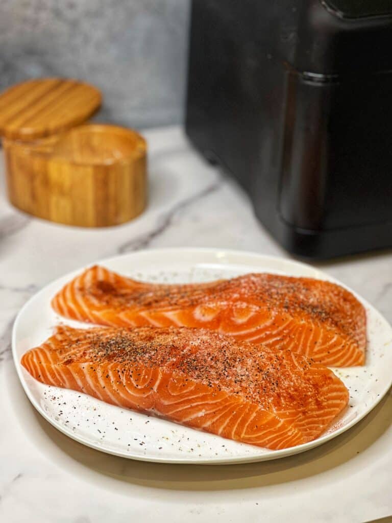 Two thick seasoned salmon filets sitting on a white plate.