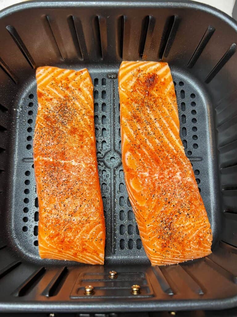 Two seasoned salmon filets sitting in an air fryer basket.