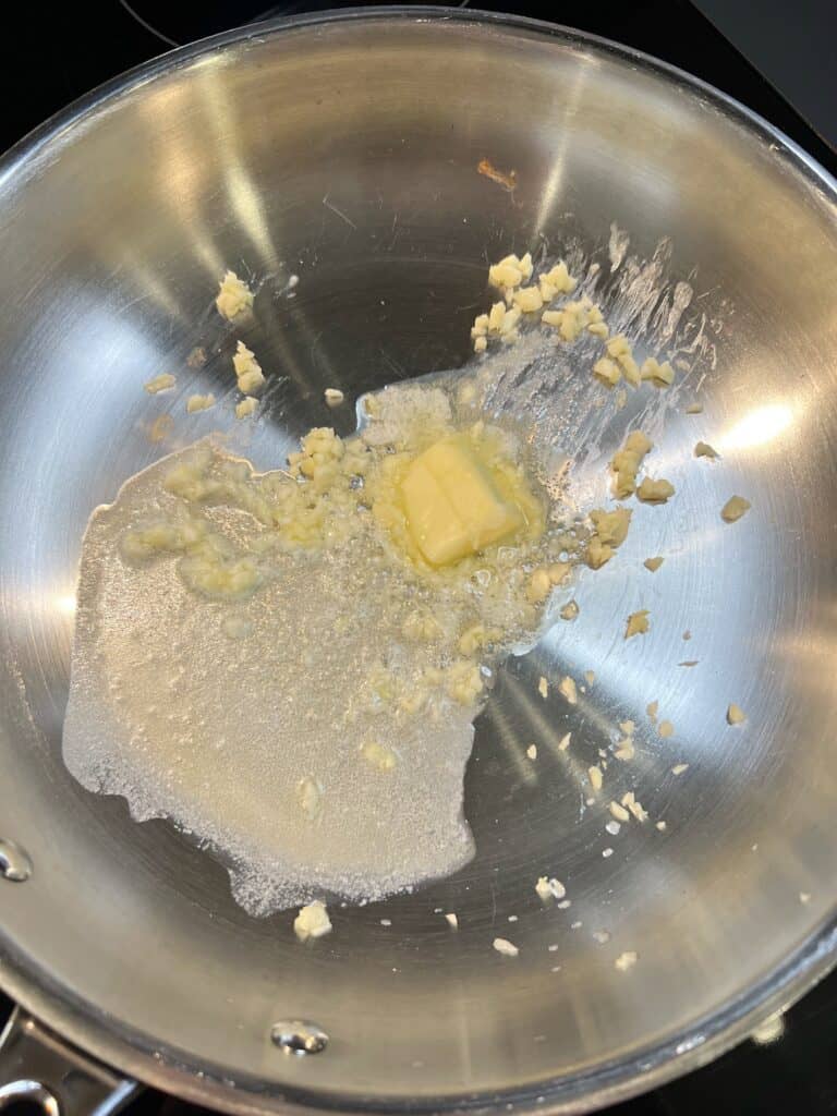 Butter melting in a stainless steel pan with minced garlic.
