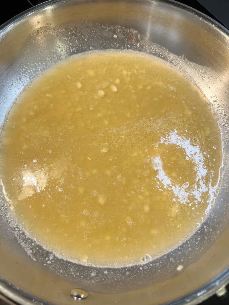 Chicken stock poured into a stainless steel pan with melted butter and minced garlic.