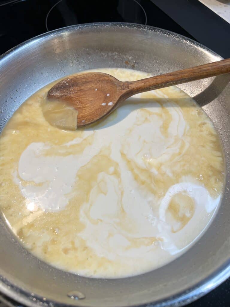 Heavy cream and Dijon mustard added to a pan of reduced chicken stock. A wooden spoon is in the pan.
