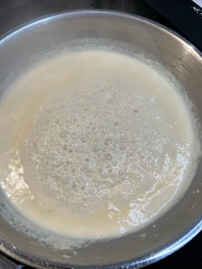 A Dijon cream sauce simmering in a stainless steel pan.