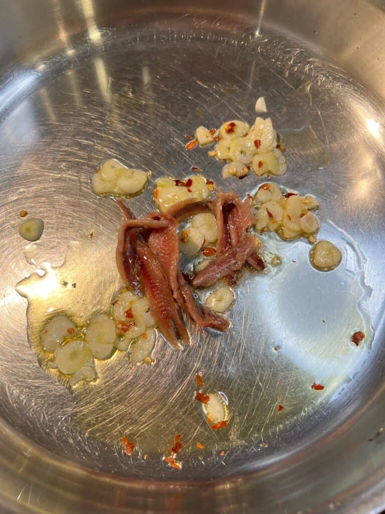 Four anchovy filets added to a pan with olive oil, sliced garlic and crushed red pepper flakes.