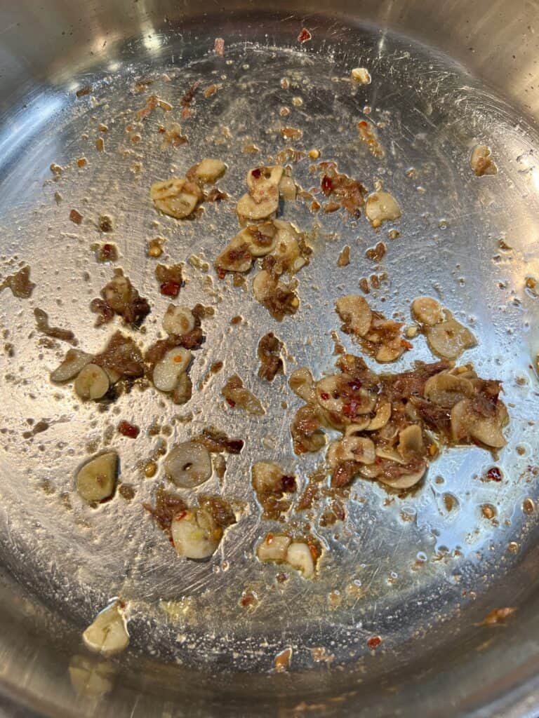 Melted anchovies in a pan with sliced garlic and crushed red pepper flakes.