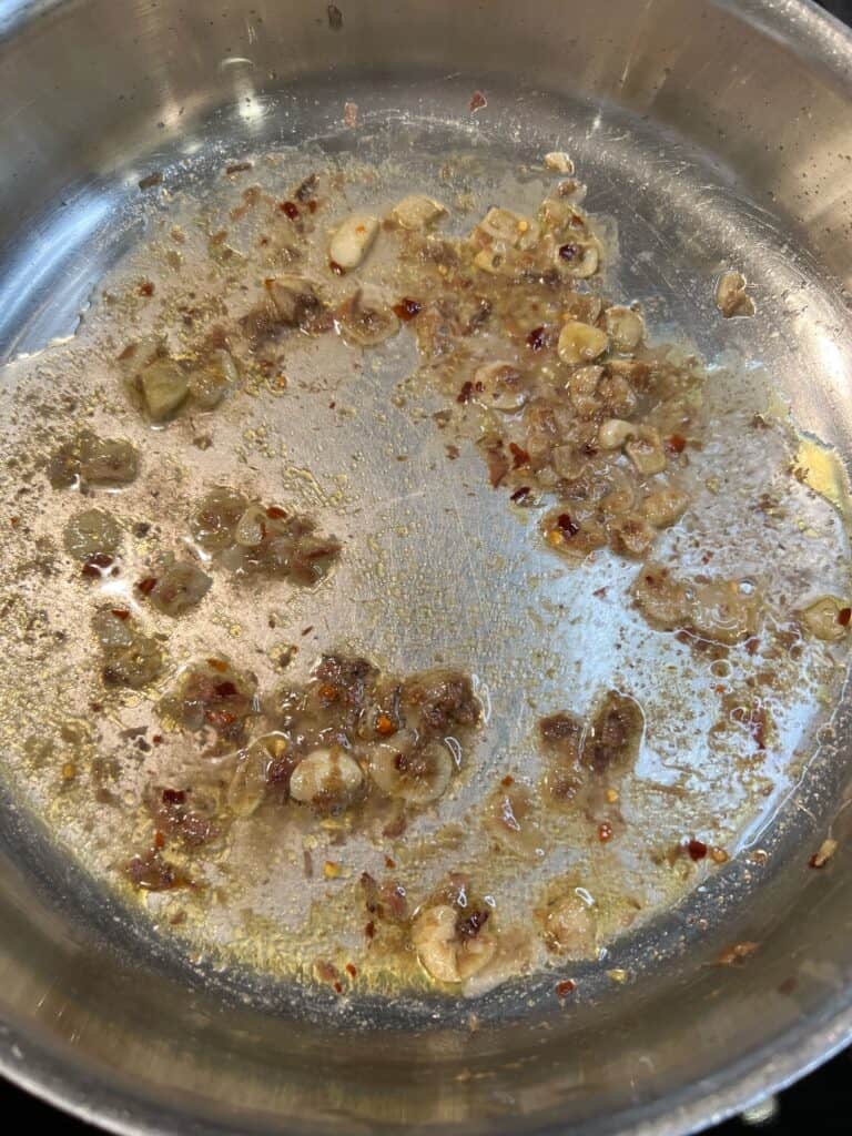White wine in a pan with melted anchovies and sliced garlic.