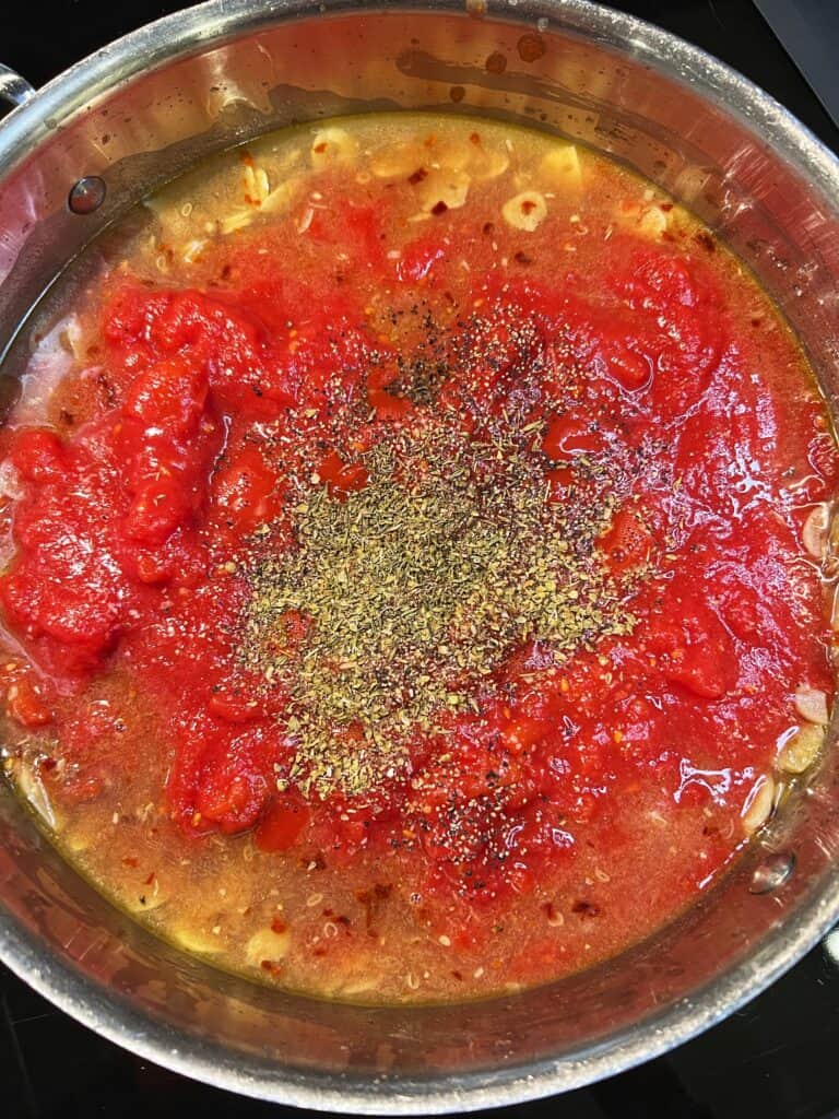 Crushed tomatoes added to a sauté pan, along with dried oregano and dried thyme.