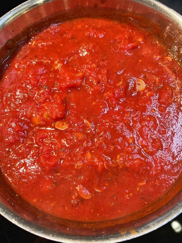 A pan of simmered puttanesca sauce. The sauce is deep red in color.