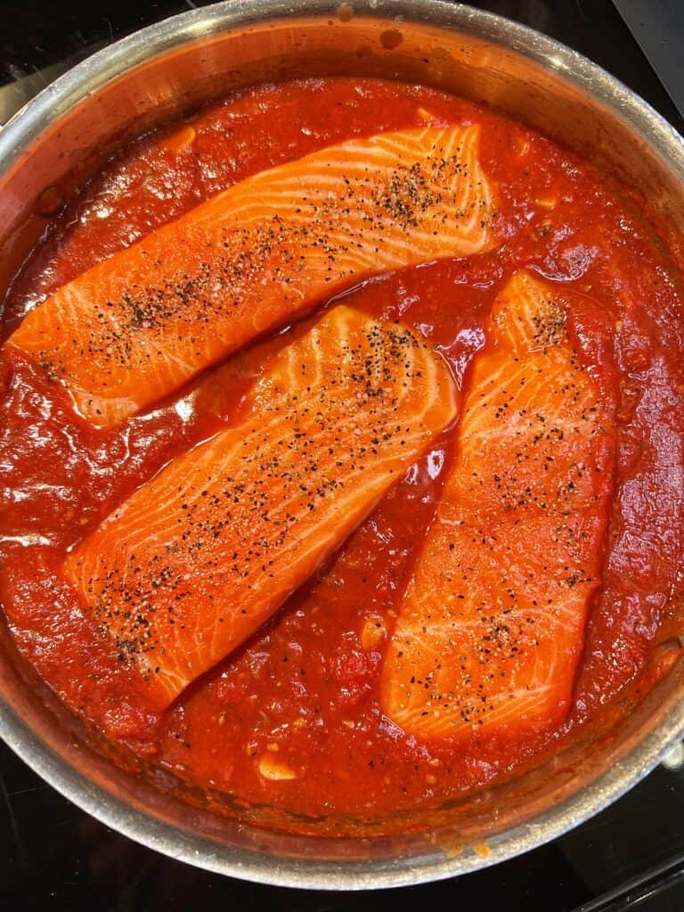 Three raw, seasoned salmon filets nestled into a red sauce.