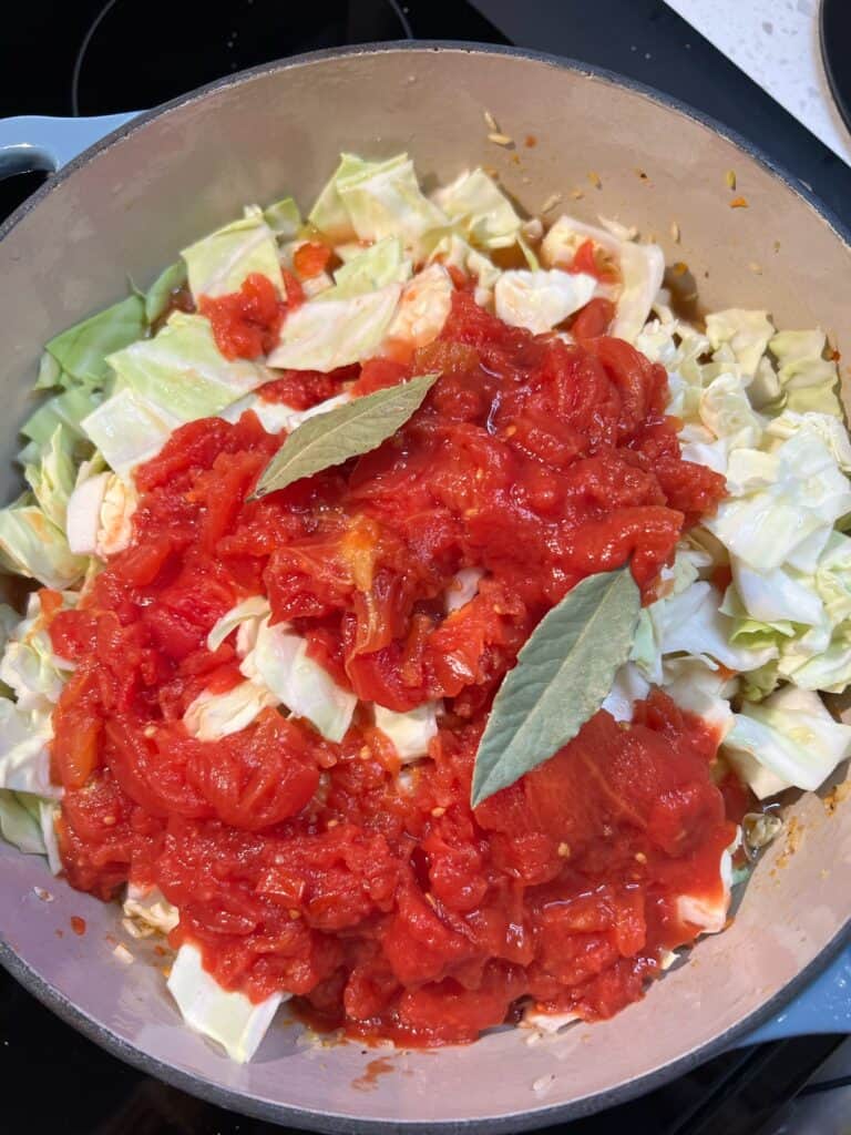 A pot of browned hot sausage, diced cabbage, crushed tomatoes and two bay leaves.