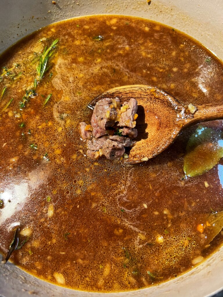 Stew meat added back to a pot with beef stock and fresh herbs.