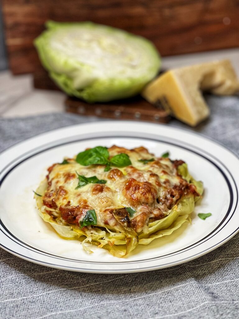 A thick sliced cabbage steak that has been baked with a meat sauce and melty cheese on top sitting on a white place trimmed with blue.