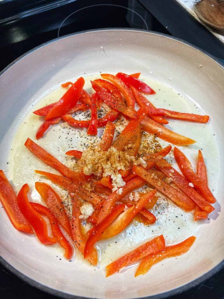 Strips of red bell pepper, minced garlic and cayenne pepper sautéing in a pan of melted butter.