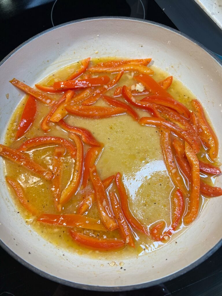 Red bell pepper strips in a pan with chicken stock.