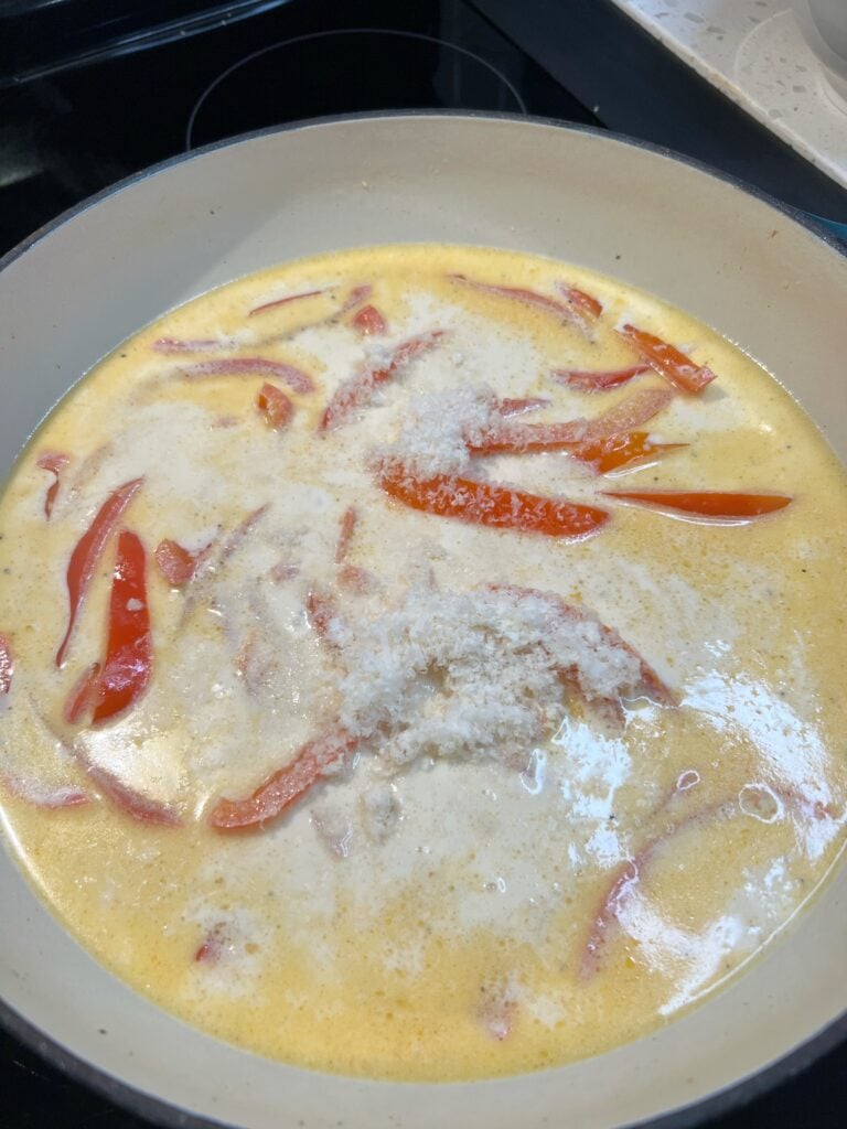 Heavy cream and grated Parmesan cheese added to a pan with sautéed strips of red bell pepper and chicken stock for Creamy Cayenne Shrimp Pasta.