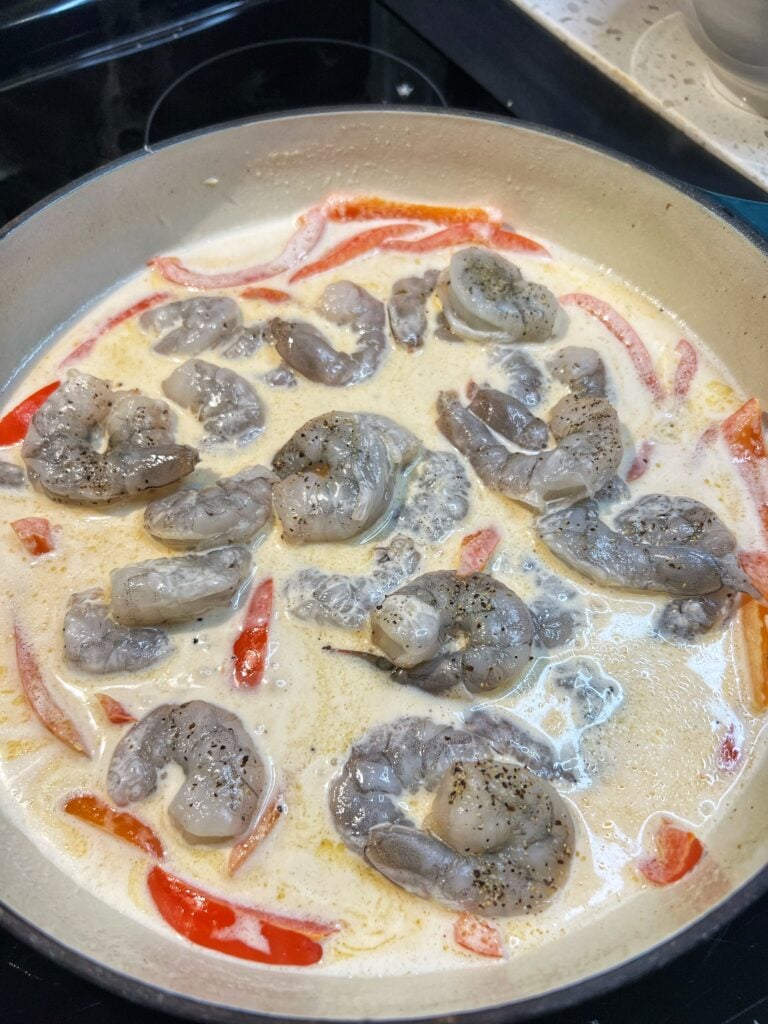 Raw shrimp added to a pan of red pepper cayenne cream sauce.