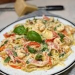 An oval white platter trimmed in black filled with Cayenne Cream Shrimp Pasta. The pasta also contains sautéed red bell peppers and fresh chopped basil.