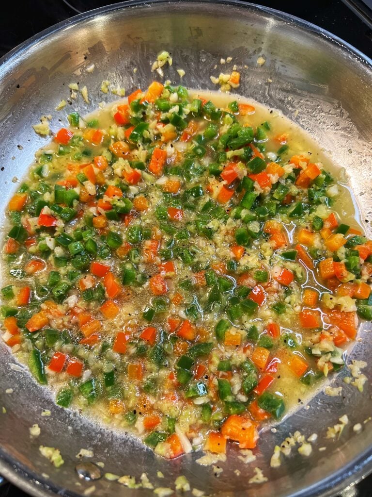 Chicken stock added to a stainless steel pan with sautéed bell peppers and onions.