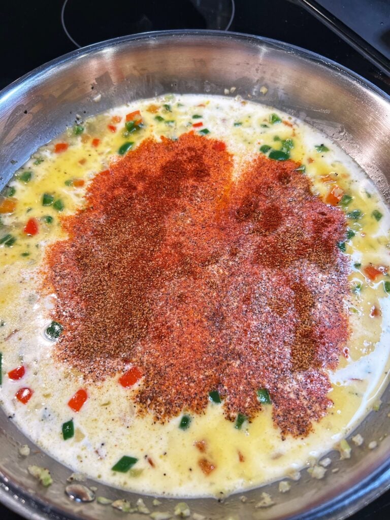 Heavy cream and Creole seasoning added to a pan of sautéed vegetables for Creole Sauce.