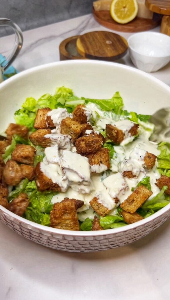 Chopped hearts of Romaine in an off-white salad bowl with homemade croutons and salad dressing poured over the top.