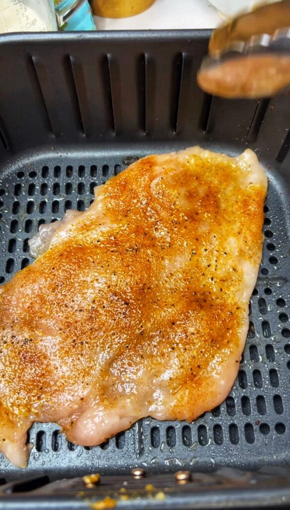 A raw, seasoned and flattened chicken breast in an air fryer basket.