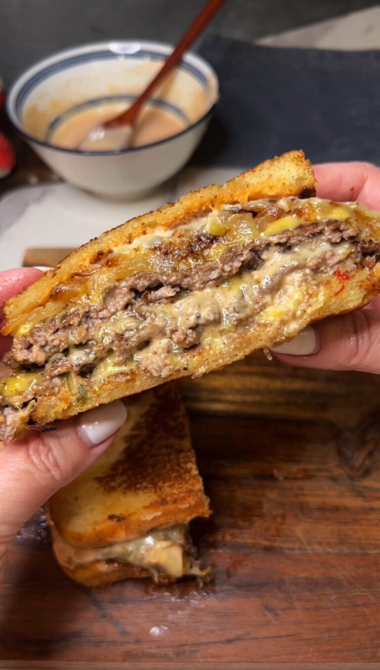 Me holding half of a patty melt with burger sauce so that you can see the inside flat cheeseburger, caramelized onions and burger sauce.