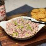A small off-white bowl holding hot honey ham salad that is garnished with chopped celery leaves. The salad has a pinkish hue from the ham that is mixed with mayo.