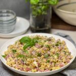 Italian Grinder Pasta Salad in a flat, white bowl. The salad is made up of cooked ditalini pasta, diced deli meats, diced cheese, banana peppers and fresh basil.