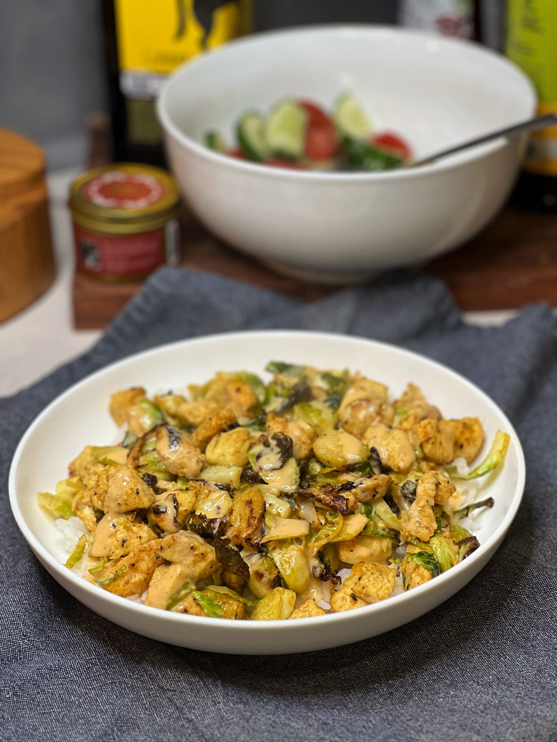 A shallow white bowl filled with chicken and Brussels sprouts over steamed white rice. The chicken is cubed and the sprouts are sliced.