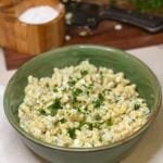 A creamy elbow macaroni salad in a green bowl. The salad is garnished with fresh chopped parsley.