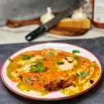 A piece of chicken Parmesan alla vodka on a white plate. A piece of crispy chicken is covered in a orangish sauce that had melted mozzarella on top. The dish is garnished with fresh basil.