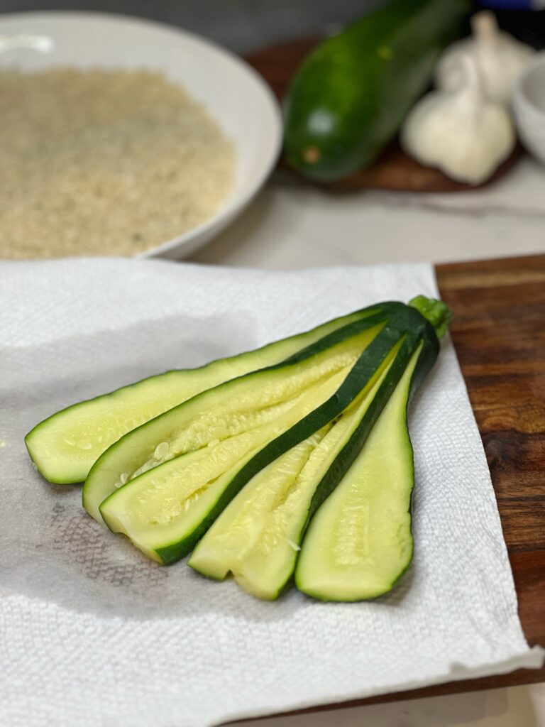 A fresh zucchini that has been softened in the microwave and cut to fan out, but is still attached to the stem. The fanned zucchini is laying on paper towels.