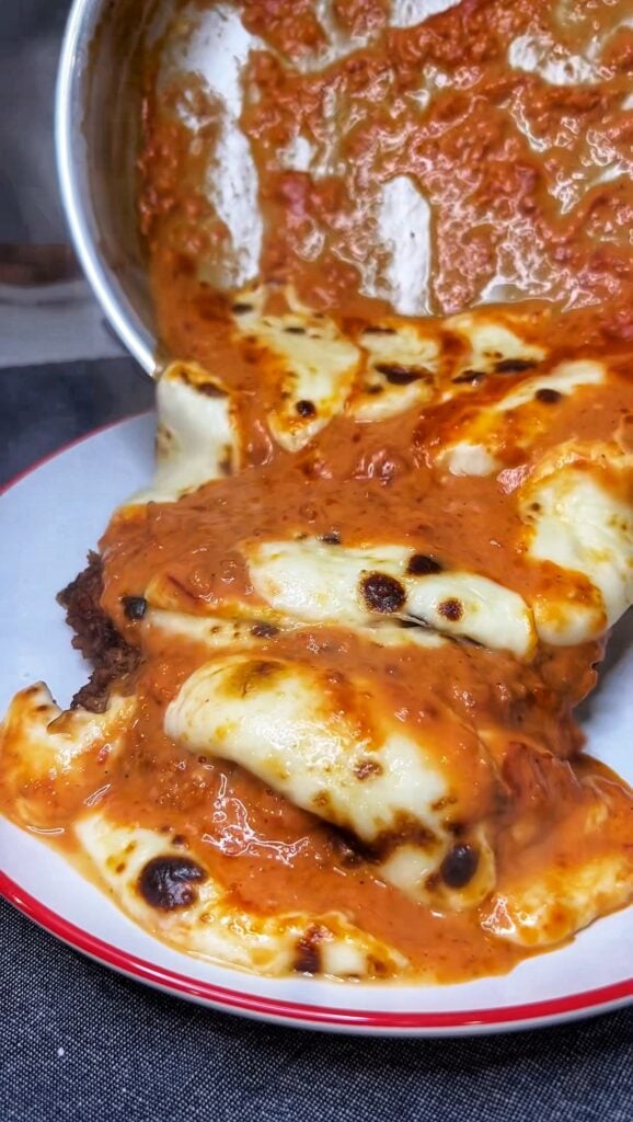 Pouring a vodka cheese sauce on top of a crispy chicken cutlet.