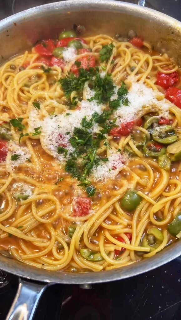 Overhead shot of a one pan pasta puttanesca. Cooked spaghetti with olives, capers, cooked down cherry tomatoes and Parmesan cheese.