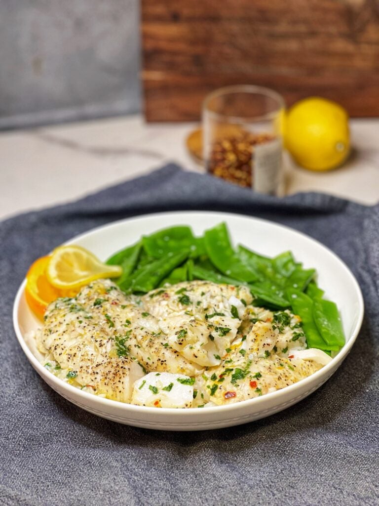A white bowl holding citrus baked fish filets, steamed rice and snow peas.