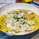 A blue enameled cast iron casserole filled with baked citrus fish and garnished with fresh chopped parsley.