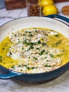 A blue enameled cast iron casserole filled with baked citrus fish and garnished with fresh chopped parsley.
