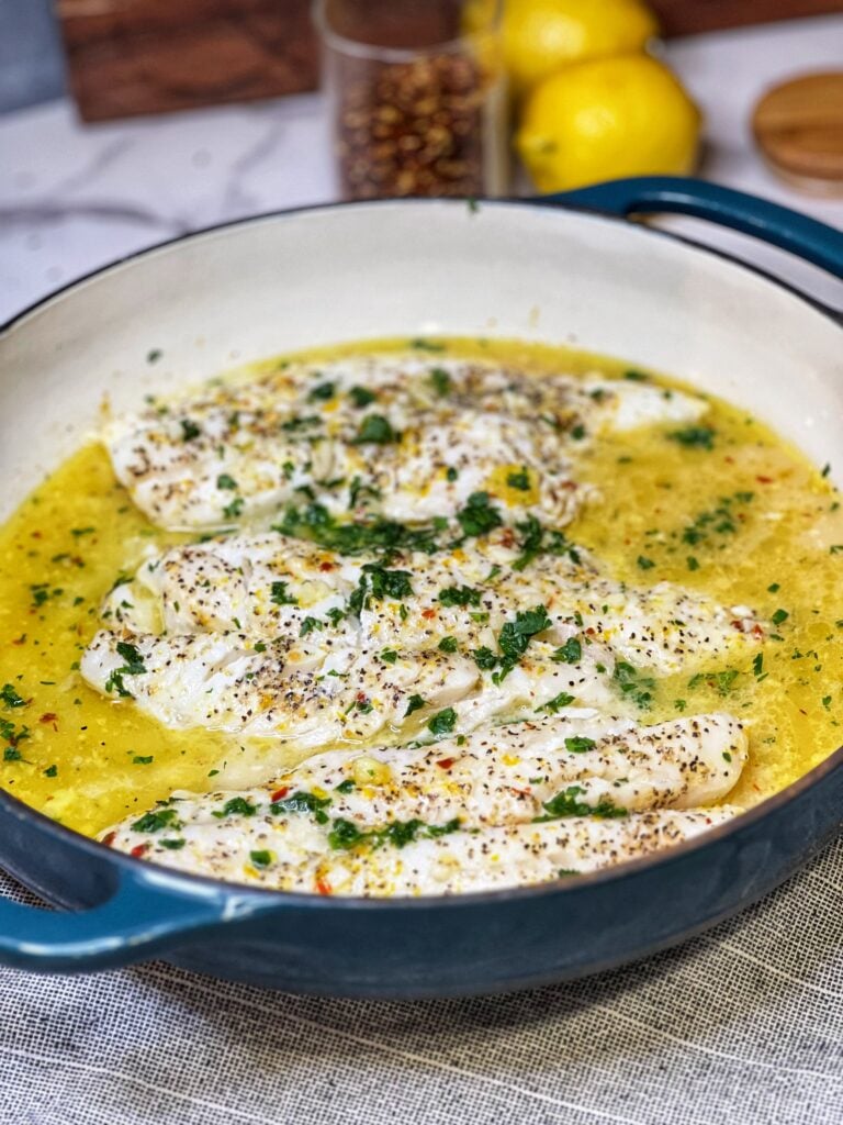 A blue enameled cast iron casserole filled with baked citrus fish and garnished with fresh chopped parsley.