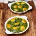 Two white escargot platters holding baked escargot with garlic butter sauce. Each escargot is topped with a small, golden puff pastry round.