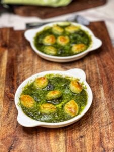 Two white escargot platters holding baked escargot with garlic butter sauce. Each escargot is topped with a small, golden puff pastry round.