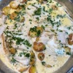 An over the top view of a pan of cod with rosemary cream sauce and roasted potatoes.