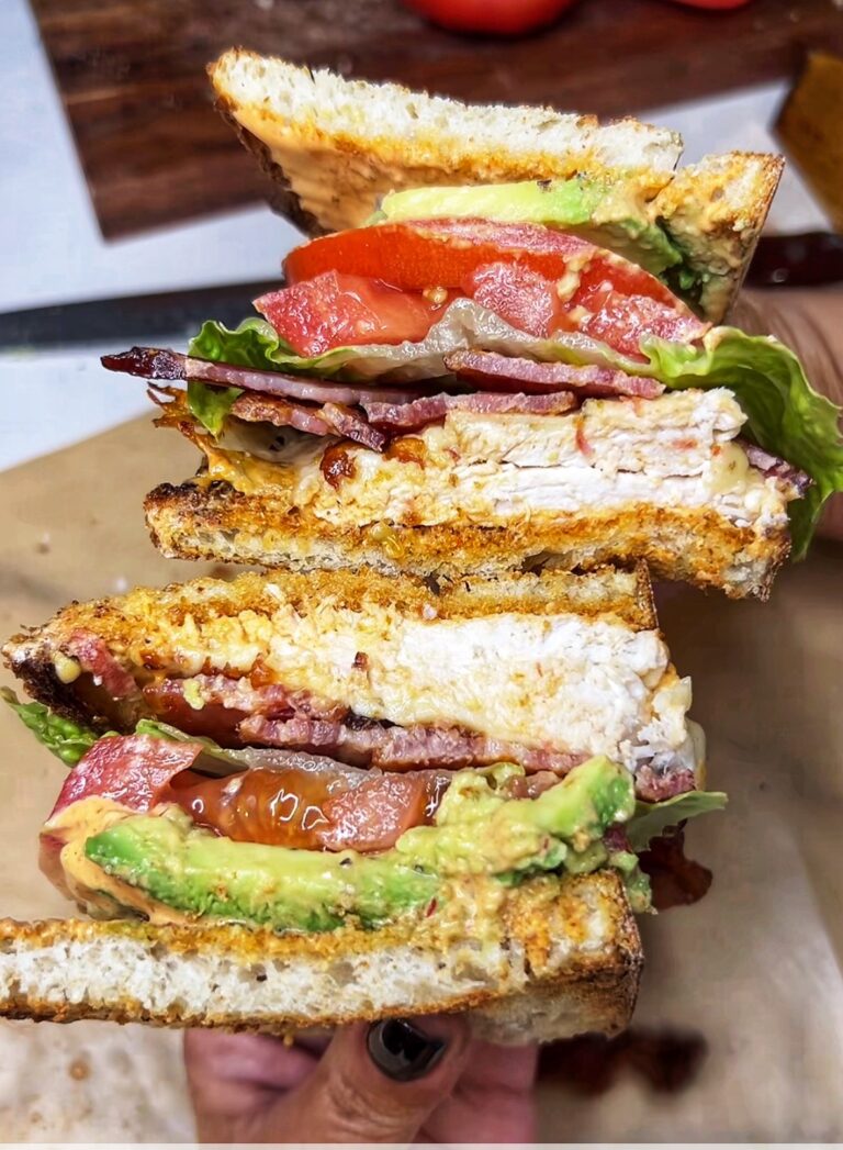 Me holding two halves of a Spicy Chicken BLT Sandwich kind of stacked on each other. Showing are the inside cut portions with the spicy mayo, avocado, chicken, bacon and Romaine lettuce.