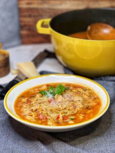 A bowl of chicken and orzo soup. The soup is tomato-based and is garnished with fresh basil and grated Parmesan cheese.
