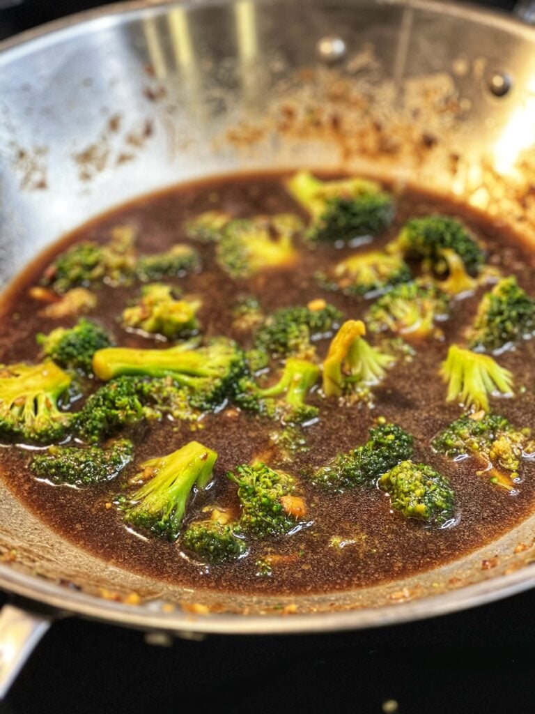 Cut broccoli in a wok with a brown sauce.