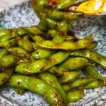 Sweet and Spicy Edamame in a bowl. The edamame are steamed in pods and mixed with a spicy sauce.