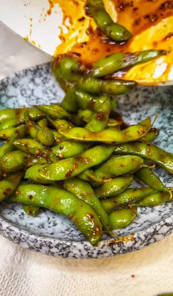 Sweet and Spicy Edamame in a bowl. The edamame are steamed in pods and mixed with a spicy sauce.