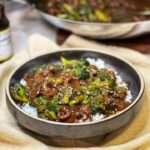 A brown bowl filled with steamed rice and topped with beef and broccoli. The dish is garnished with toasted sesame seeds.