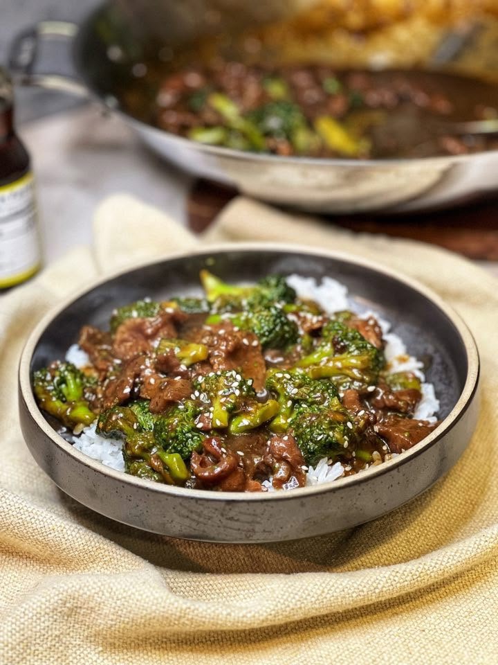 A brown bowl filled with steamed rice and topped with beef and broccoli. The dish is garnished with toasted sesame seeds.