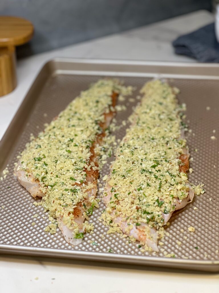 A sheet pan holding to big filets of wolffish that are coated in a panko and almond breadcrumb mixture ready to be baked.