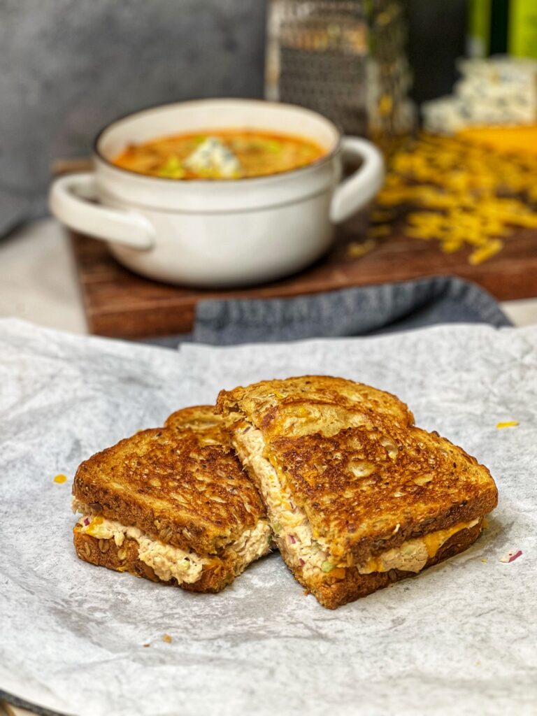 A classic tuna melt sandwich cut in half with one side slightly on top of the other sitting on a piece of white parchment paper.
