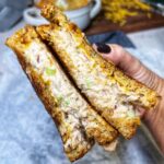 Me holding two halves of a classic tuna melt sandwich. The inside of the sandwich with melty cheese and tuna salad is facing front. The grainy bread is toasted.